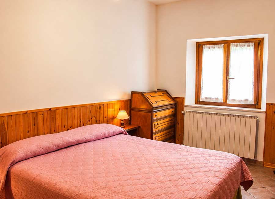 Appartamento Opi La Sosta con camera tripla luminosa, copriletto rosa, finestra e mobili in legno.