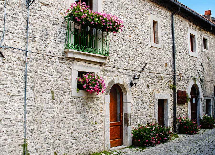 Cosa fare a Opi, vicolo del borgo storico con case in pietra, balconi fioriti e atmosfera autentica di montagna.